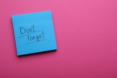 Photo of Paper note with phrase Don't Forget on pink background, top view. Space for text