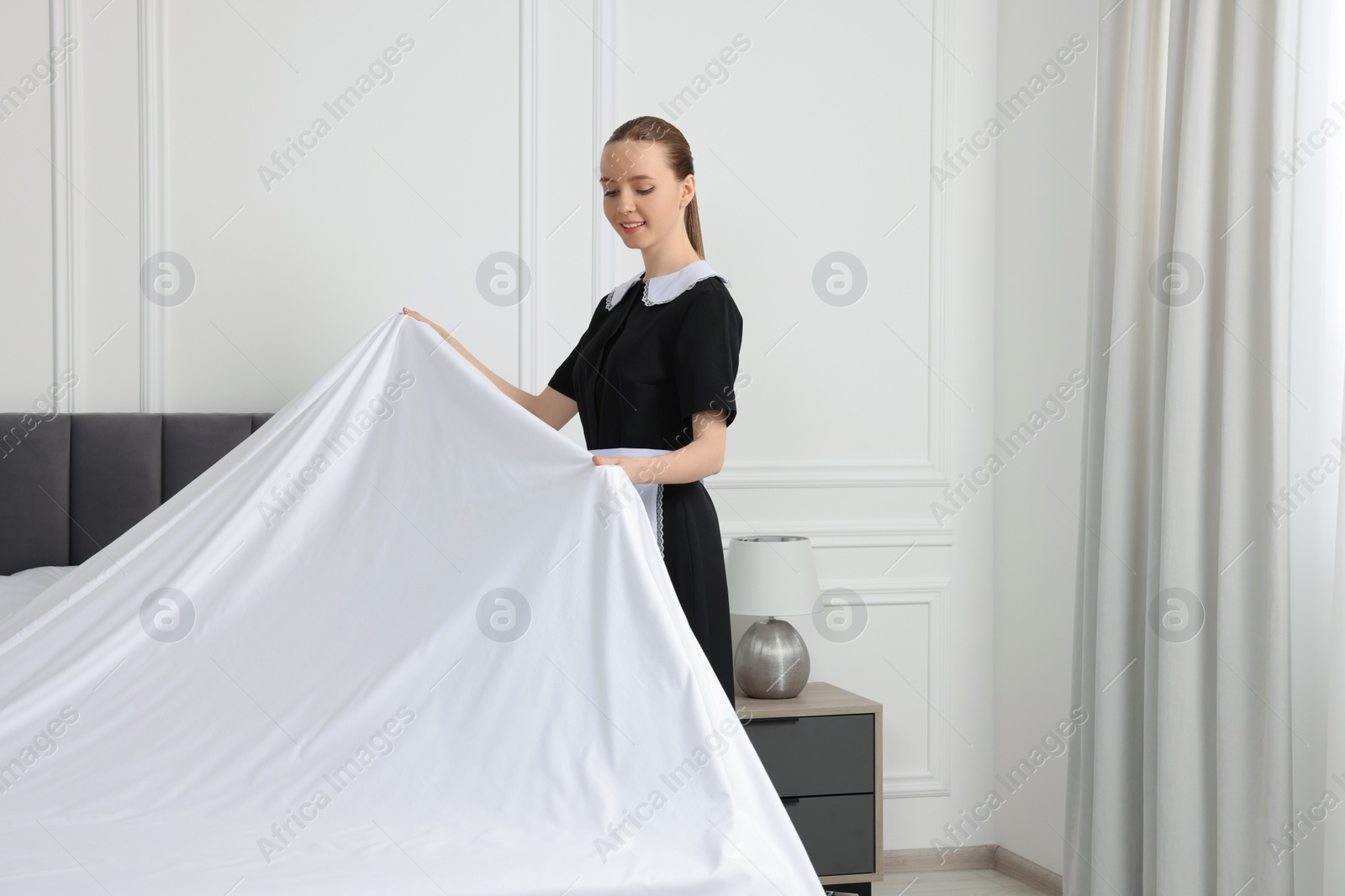 Photo of Young maid making bed in hotel room