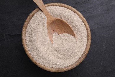 Photo of Bowl and spoon with active dry yeast on black table, top view