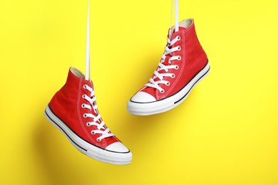 Photo of Pair of new stylish red sneakers hanging on laces against yellow background