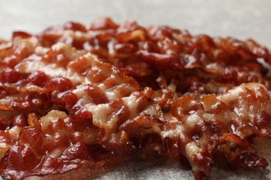 Photo of Pieces of tasty fried bacon on gray table, closeup