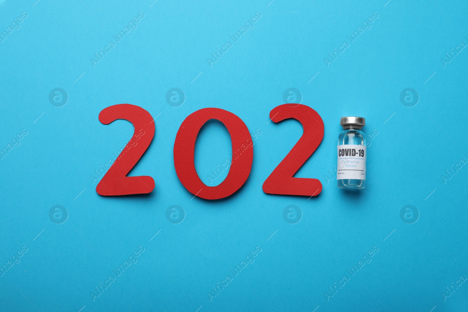 Photo of Paper numbers vial with coronavirus vaccine forming 2021 on light blue background, flat lay