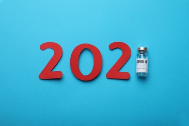 Photo of Paper numbers vial with coronavirus vaccine forming 2021 on light blue background, flat lay