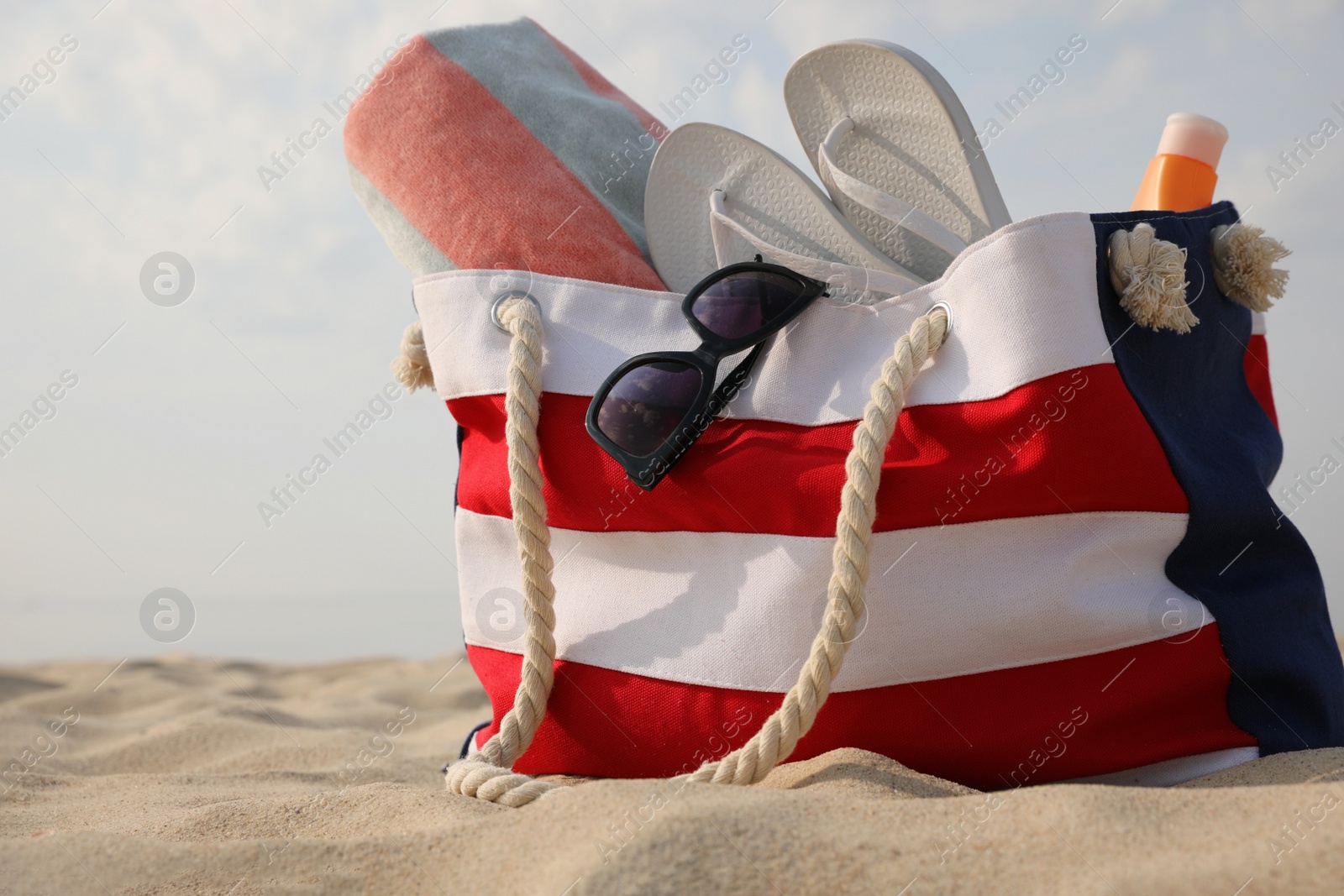 Photo of Beach bag with flip flops, towel, sunglasses and sunscreen on sand