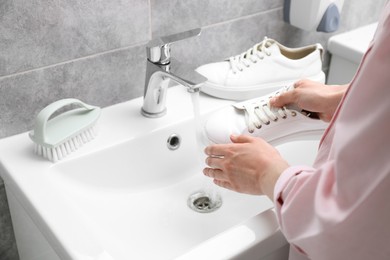 Photo of Woman washing stylish sneakers in sink, closeup