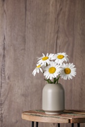 Photo of Beautiful tender chamomile flowers in vase on table against wooden background