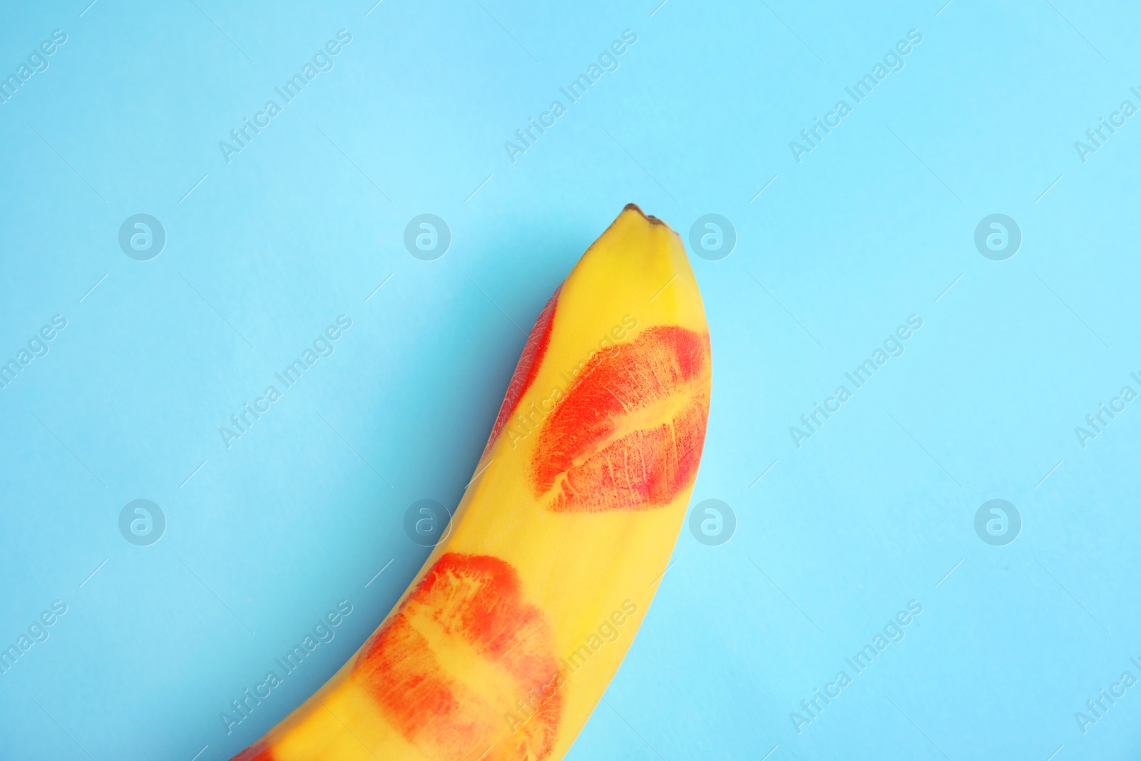 Photo of Top view of fresh banana with red lipstick marks on blue background. Oral sex concept
