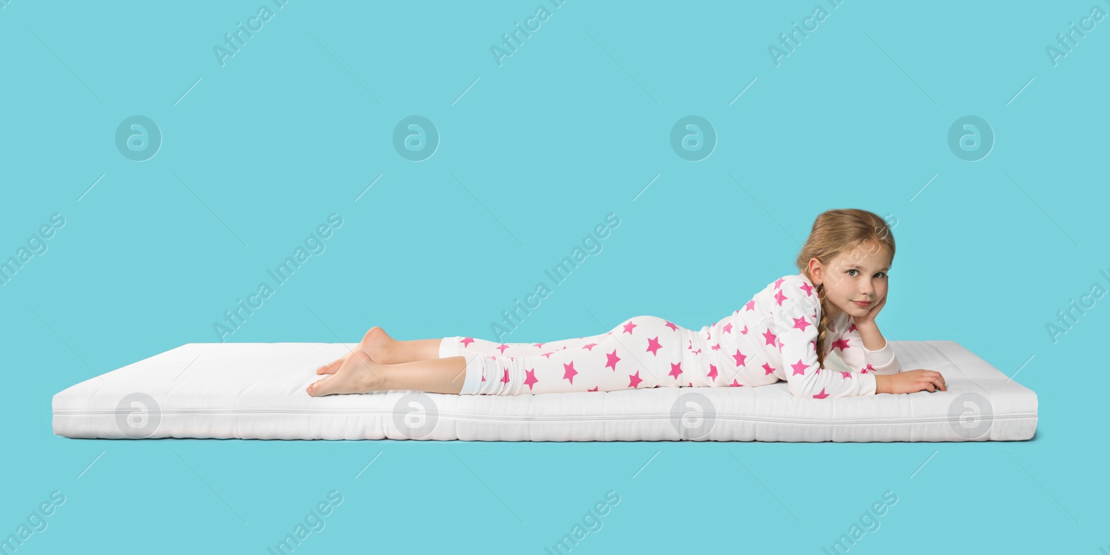 Photo of Little girl lying on comfortable mattress against light blue background, space for text