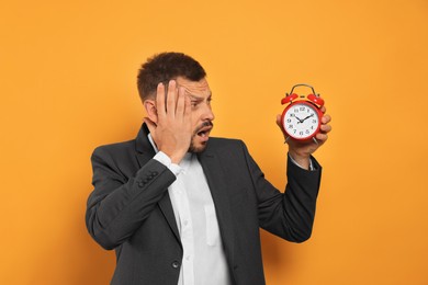 Emotional man with alarm clock on orange background. Being late concept