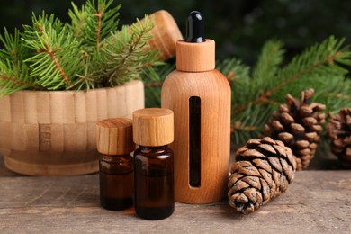 Bottles of pine essential oil, conifer tree branches and cones on wooden table