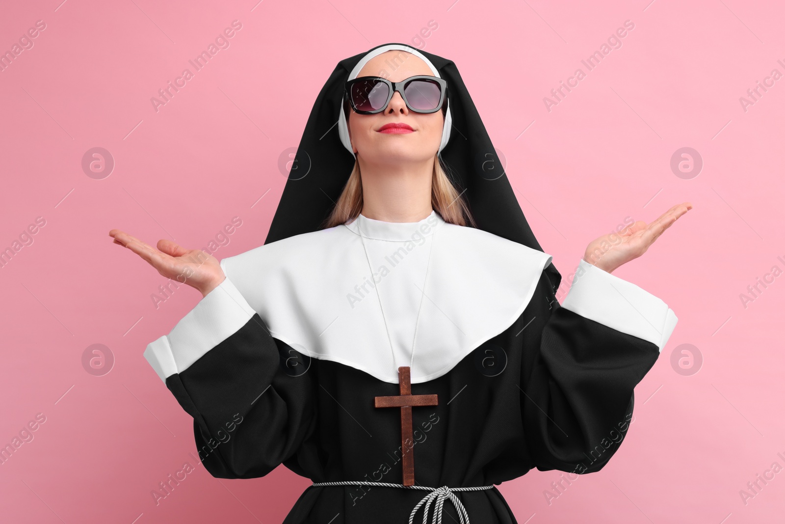 Photo of Woman in nun habit and sunglasses against pink background