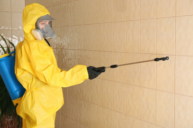 Pest control worker spraying pesticide on wall indoors