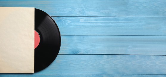 Vintage vinyl record with paper cover on blue wooden background, top view. Space for text