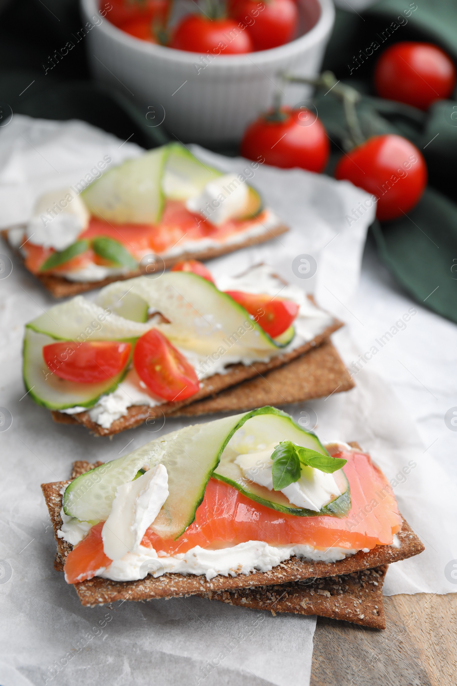 Photo of Tasty rye crispbreads with salmon, cream cheese and vegetables on parchment paper, closeup