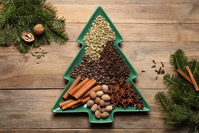 Different spices, nuts and fir branches on wooden table, flat lay