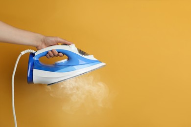 Image of Woman holding modern iron with steam on orange background, closeup. Space for text