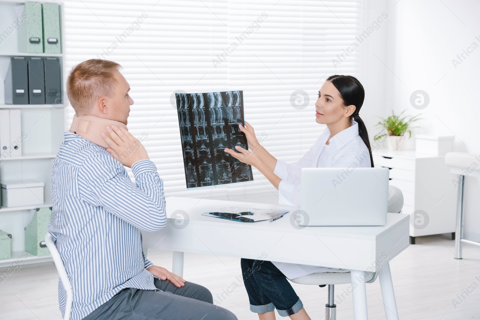 Photo of Doctor with neck MRI image consulting patient in clinic