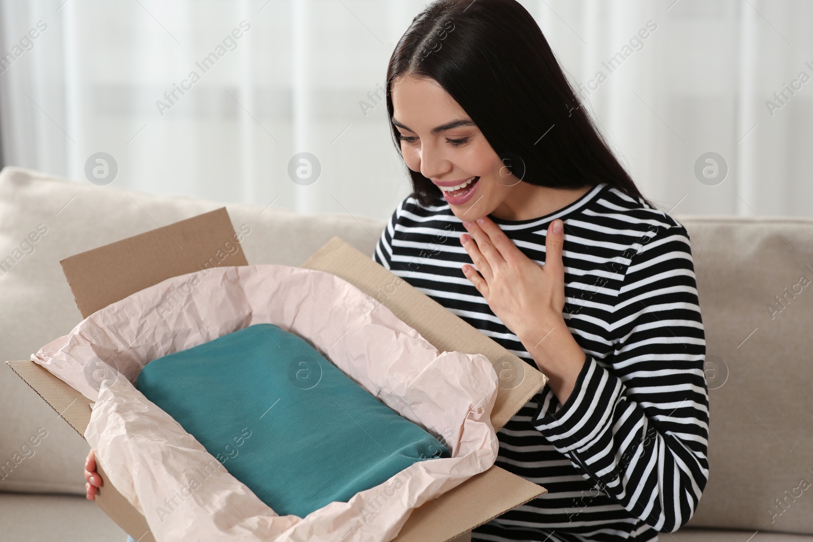 Photo of Happy woman opening parcel on sofa at home. Internet shopping