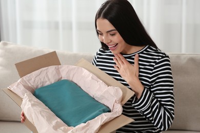 Photo of Happy woman opening parcel on sofa at home. Internet shopping