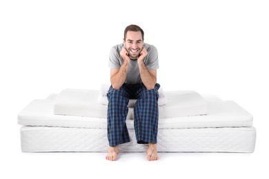 Young man sitting on mattress pile against white background