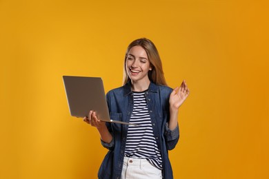 Portrait of young woman with modern laptop on yellow background
