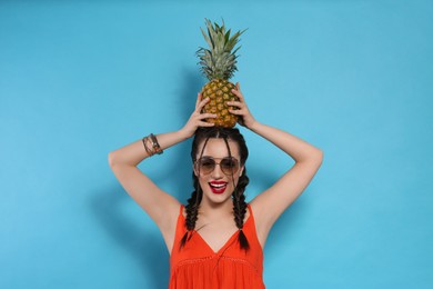 Photo of Young woman with fresh pineapple on light blue background. Exotic fruit