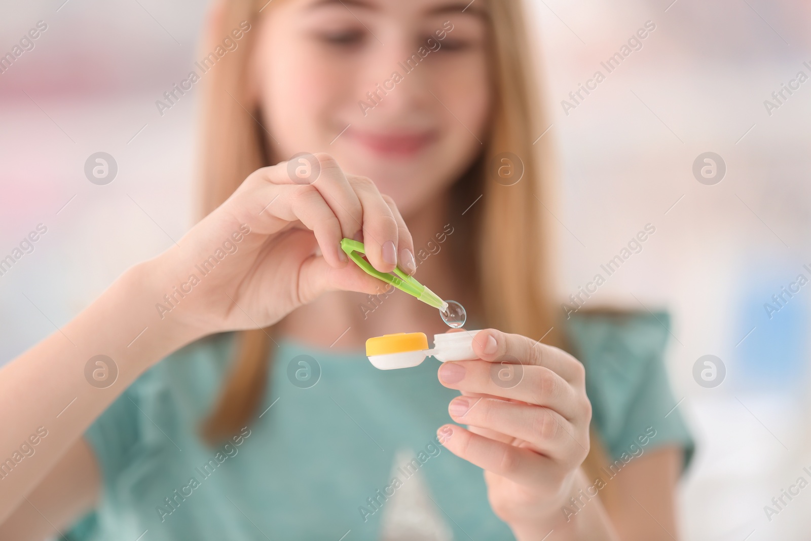 Photo of Teenage girl taking contact lens from container on blurred background