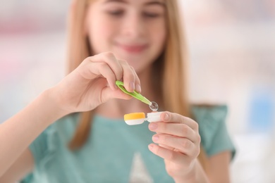 Photo of Teenage girl taking contact lens from container on blurred background