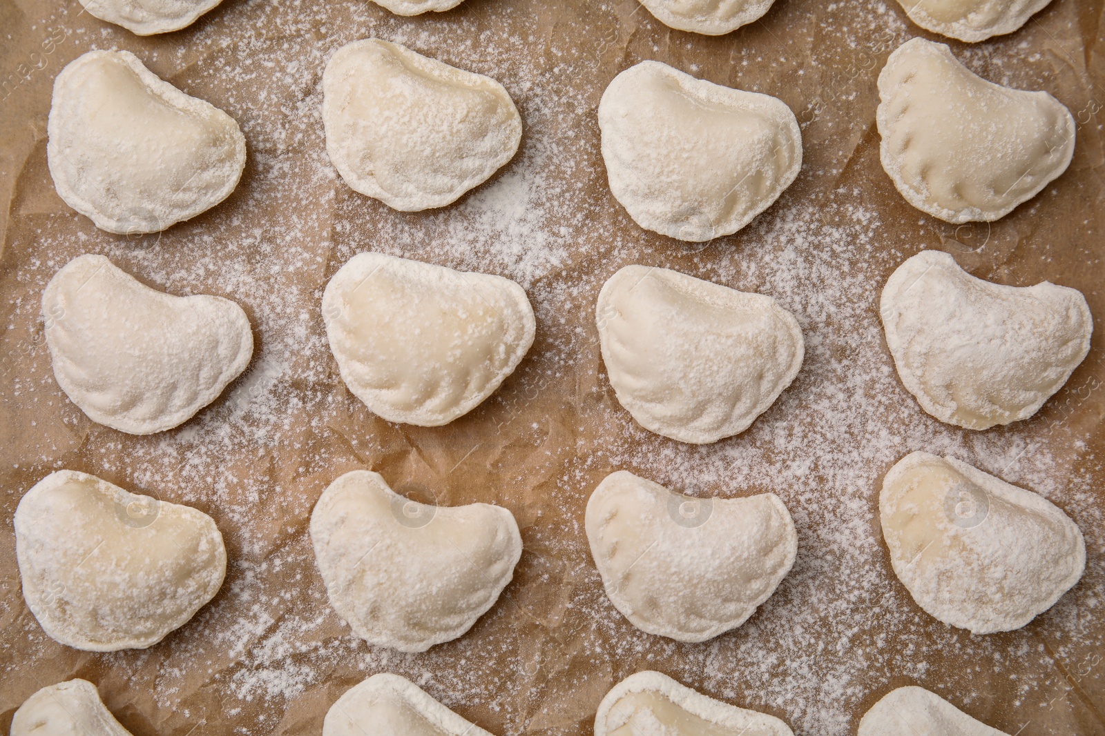 Photo of Raw dumplings (varenyky) with tasty filling and flour on parchment paper, top view