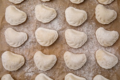 Photo of Raw dumplings (varenyky) with tasty filling and flour on parchment paper, top view