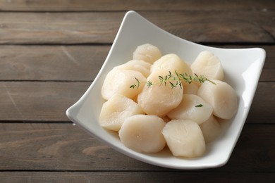 Photo of Fresh raw scallops and thyme in bowl on wooden table. Space for text
