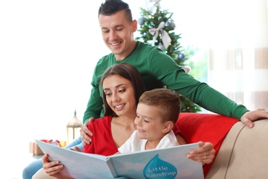 Photo of Happy parents and child reading fairy tales together at home on Christmas day