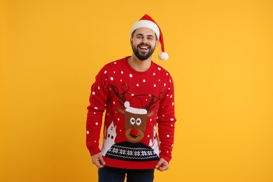 Photo of Happy young man in Christmas sweater and Santa hat on orange background