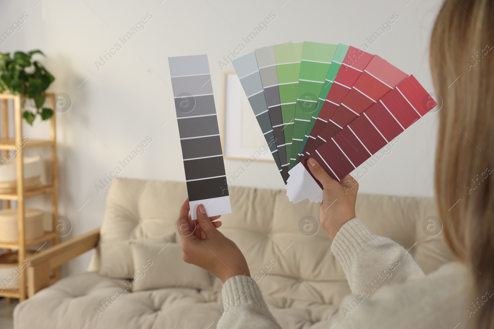 Photo of Woman choosing color for wall in room, focus on hands with paint chips. Interior design