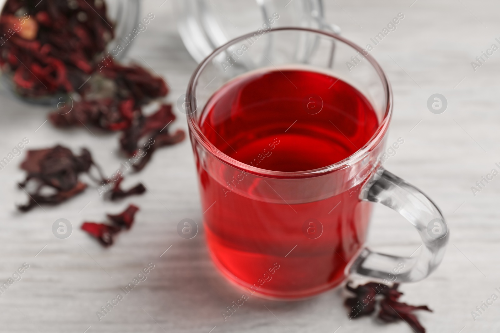 Photo of Delicious hibiscus tea and dry flowers on white wooden table, closeup