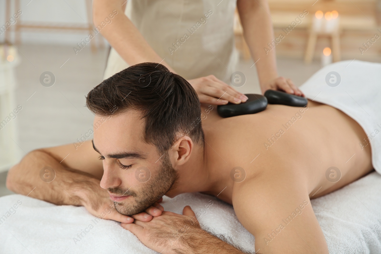 Photo of Handsome man receiving hot stone massage in spa salon