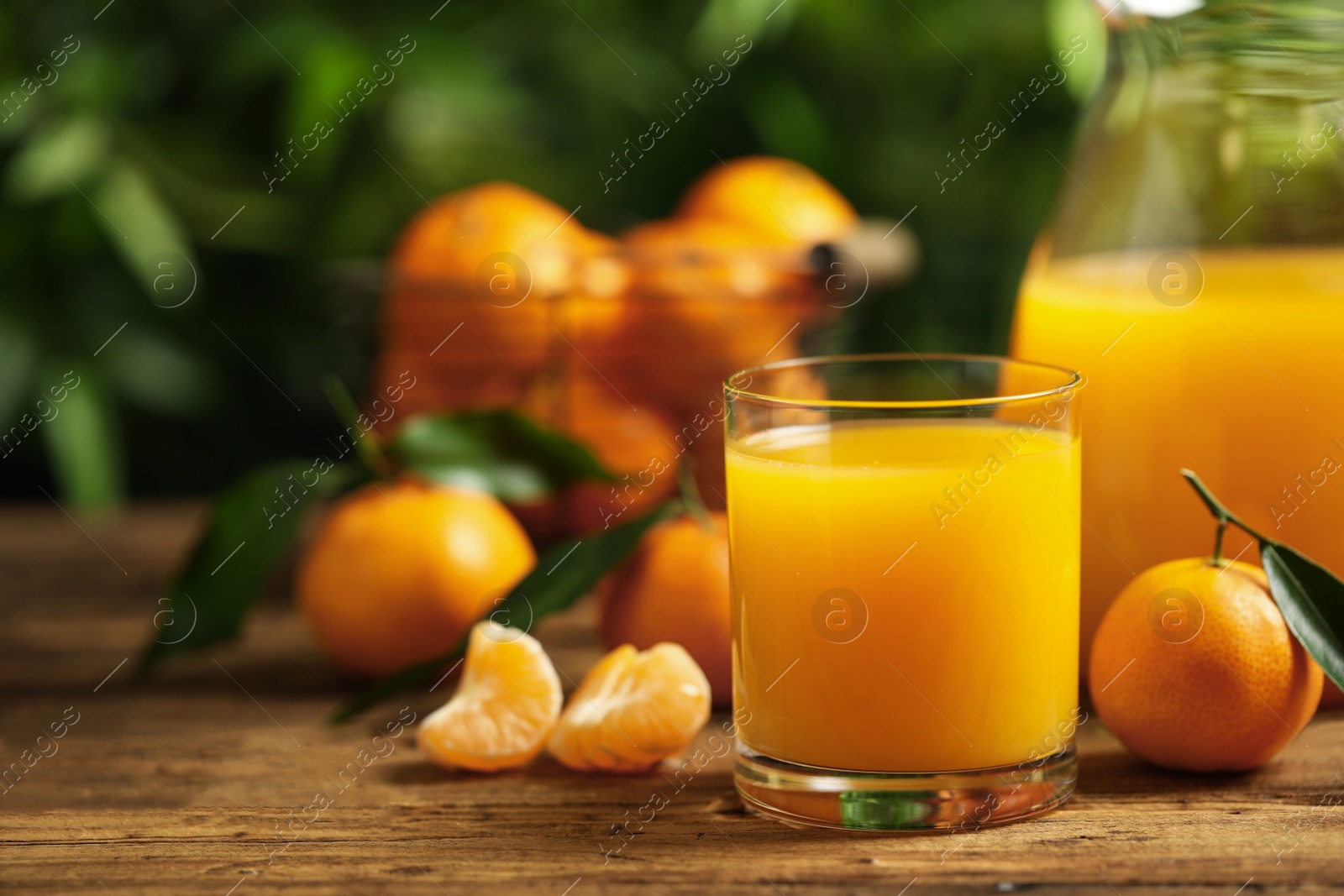 Photo of Glass and bottle of fresh tangerine juice and fruits on wooden table