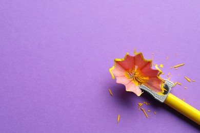 Photo of Yellow pencil, sharpener and shavings on violet background, flat lay. Space for text