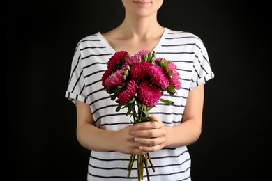 Woman with bouquet of beautiful asters on black background, closeup. Autumn flowers