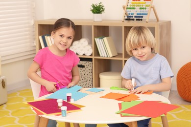 Girl cutting colorful paper and boy using glue stick at desk in room. Home workplace