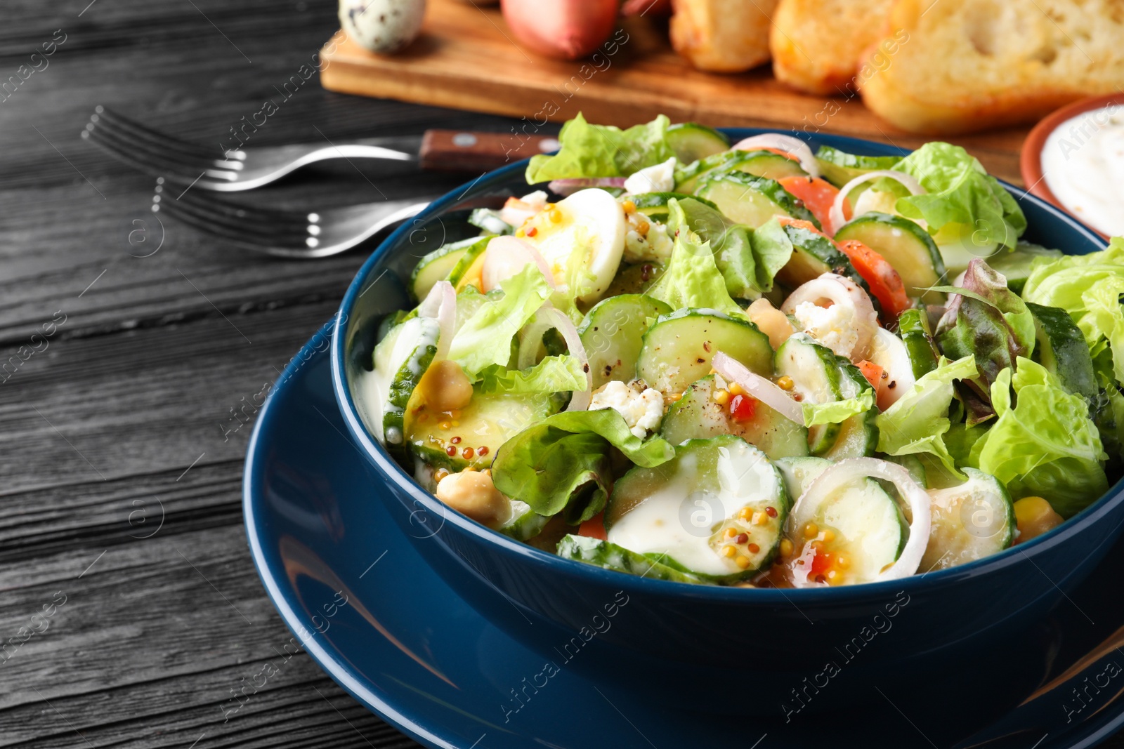 Photo of Bowl of delicious cucumber salad served on black wooden table, closeup