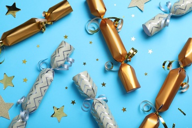 Photo of Christmas crackers and shiny confetti on light blue background, flat lay