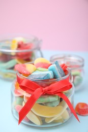 Photo of Glass jars with tasty colorful jelly candies on light blue table, closeup
