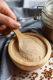 Photo of Woman taking buckwheat flour with spoon from bowl at white table, closeup