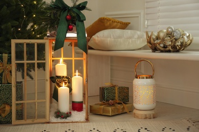 Wooden decorative lanterns with burning candles near Christmas tree in room