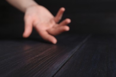 Photo of Woman holding hand above black wooden table, selective focus. Space for text