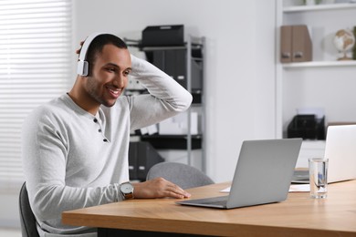 Photo of Young man with headphones working on laptop at table in office