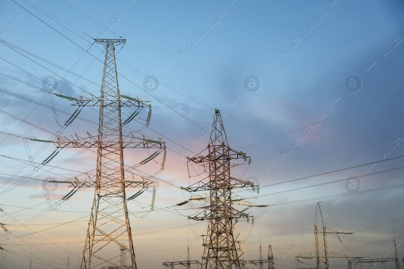 Photo of High voltage towers against cloudy sky at sunset