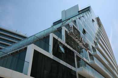 Photo of Unfinished building with swing stage against blue sky, low angle view. Construction site