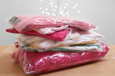 Photo of Stack of folded clothes in plastic bags on wooden table against beige background with blurred lights